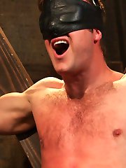 Chained to the St. Andrews Cross, Connor Patricks awaits with leather blindfold impairing his...